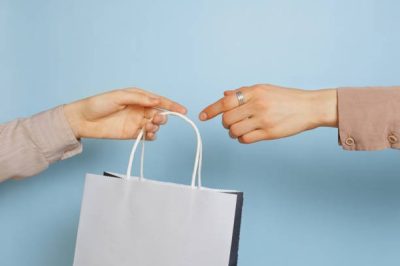 bag-handover-blue-bgd Select focus of one hand is passing a craft whiten paper bag to the other hand. Concept of thrift stores, resale, second hand.
